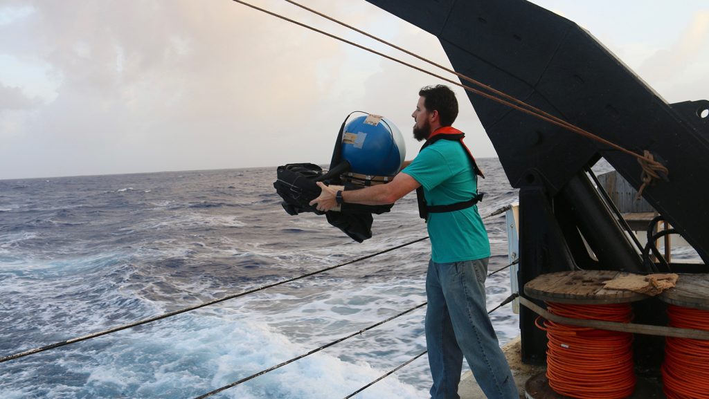 Shaun Dolk throws a packaged ocean drifter over the side of a ship toward the open sea.
