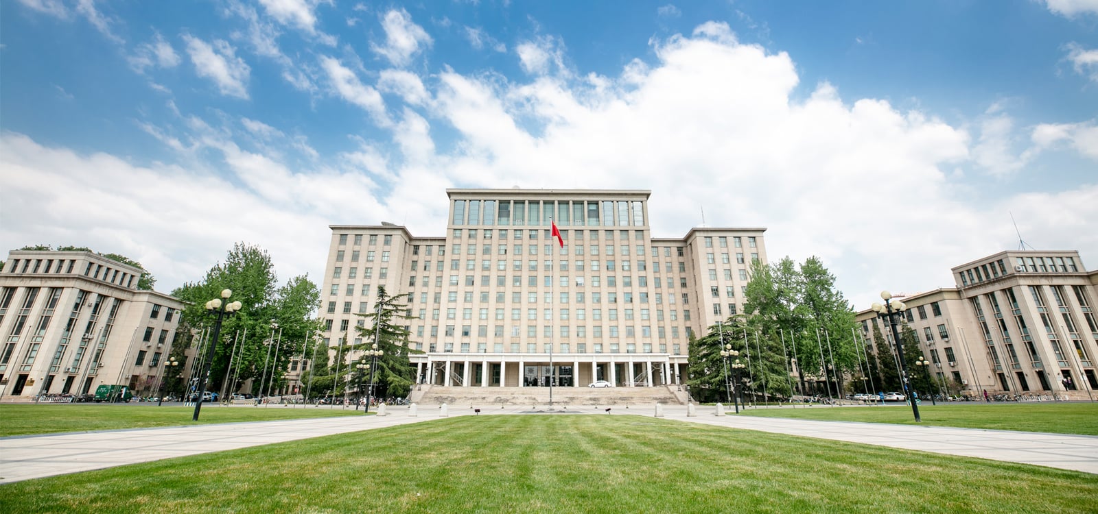 Tsinghua University main building beyond a broad lawn, with trees framing its pale stone facade.