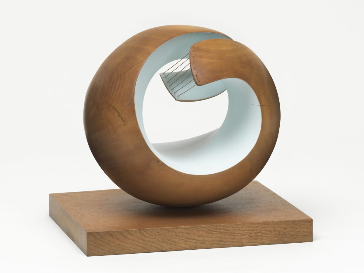Barbara Hepworth’s rounded wooden sculpture Pelagos, with a pale blue interior and strings crossing the upper part of its opening, on an oak base.