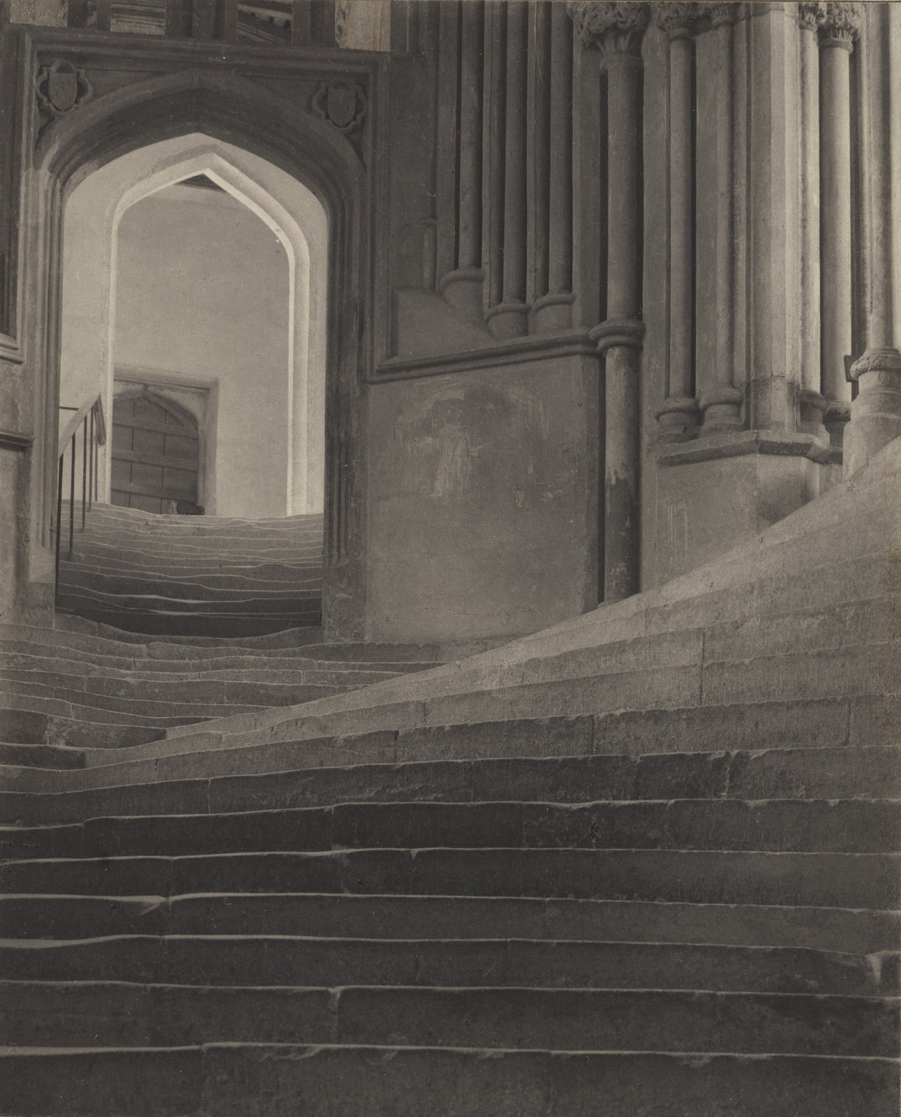 Frederick H. Evans’s photograph of worn stone stairs at Wells Cathedral, with a flight curving upward at right and another continuing through a pointed arch at left.