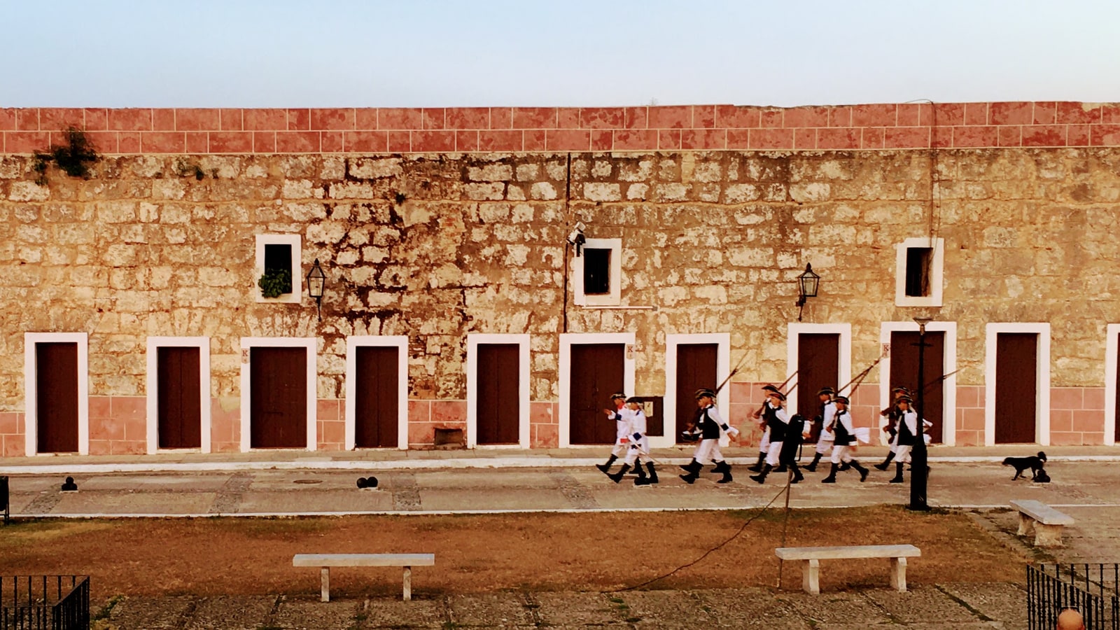 Soldiers in white trousers and dark boots march past a long weathered stone building during the ceremony at Havana’s La Cabaña fortress.