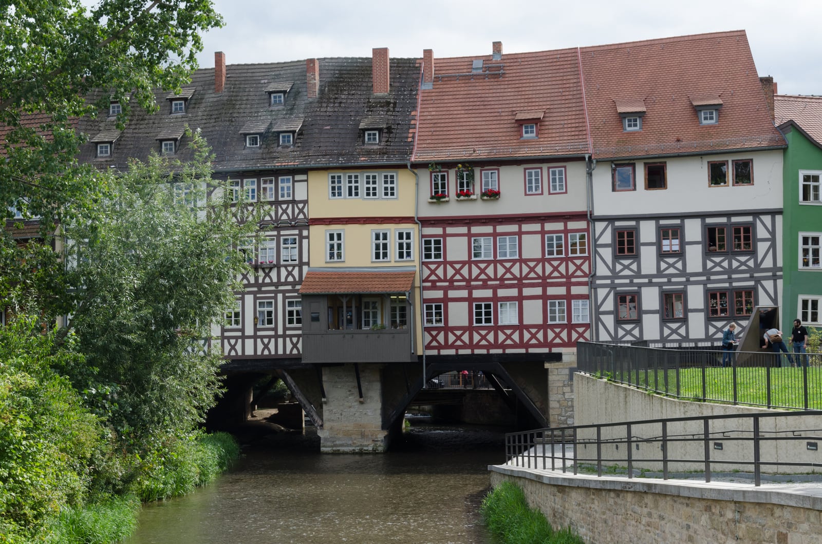 Half-timbered houses rise above the stone arches of Erfurt’s Krämerbrücke, seen from the riverbank on its north side.