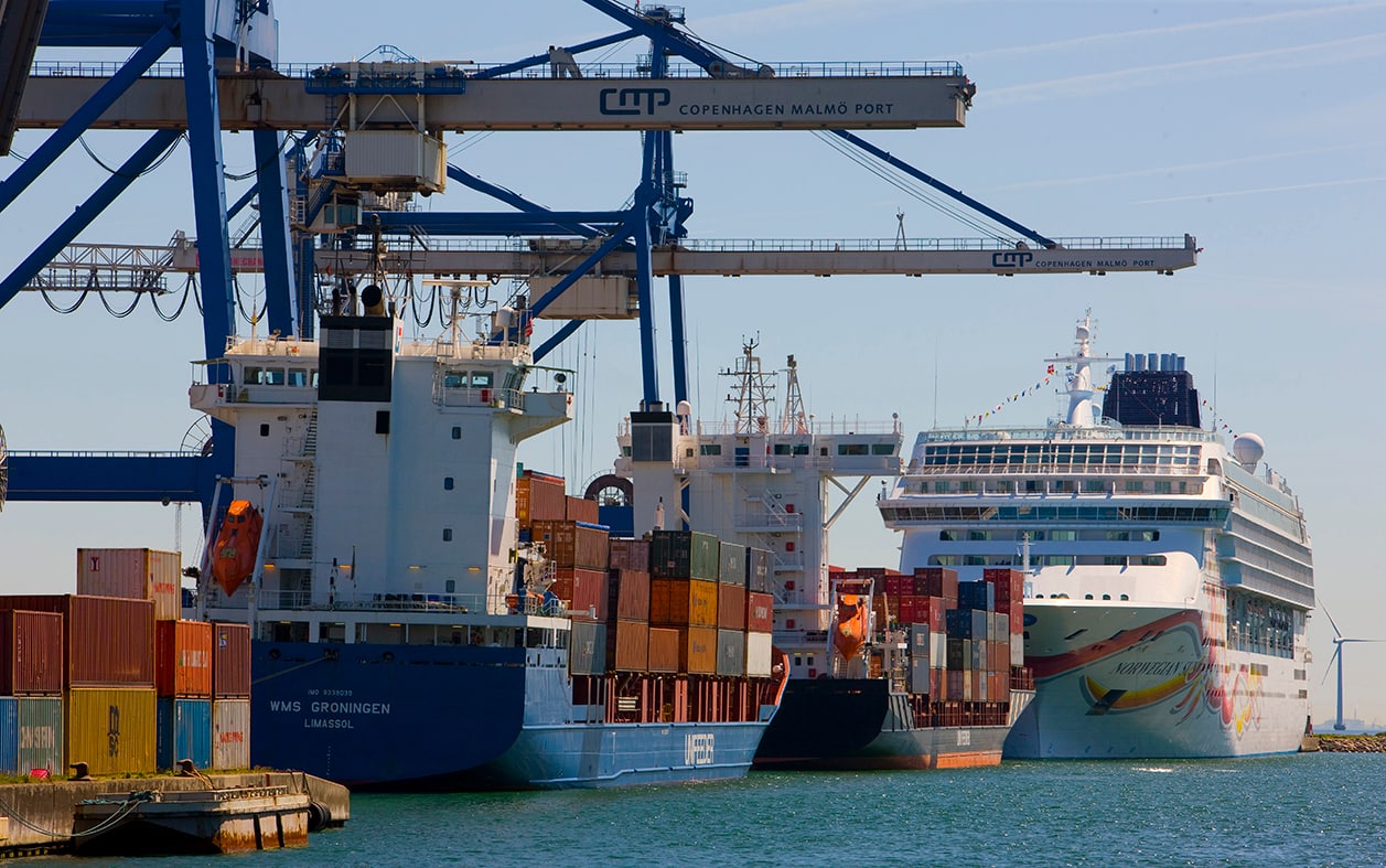 A container ship alongside a Copenhagen quay, with gantry cranes above its stacked containers.