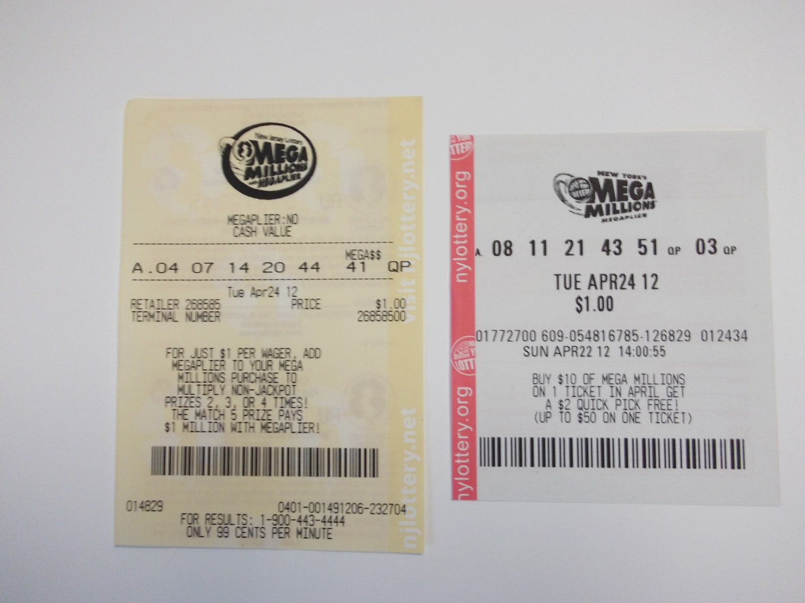 Two paper Mega Millions lottery tickets from New Jersey and New York lie side by side on a pale surface.