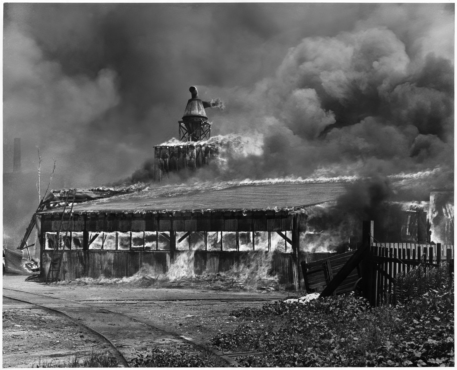 Flames spread through a low warehouse in St. Louis beneath a roof vent and thick clouds of smoke.