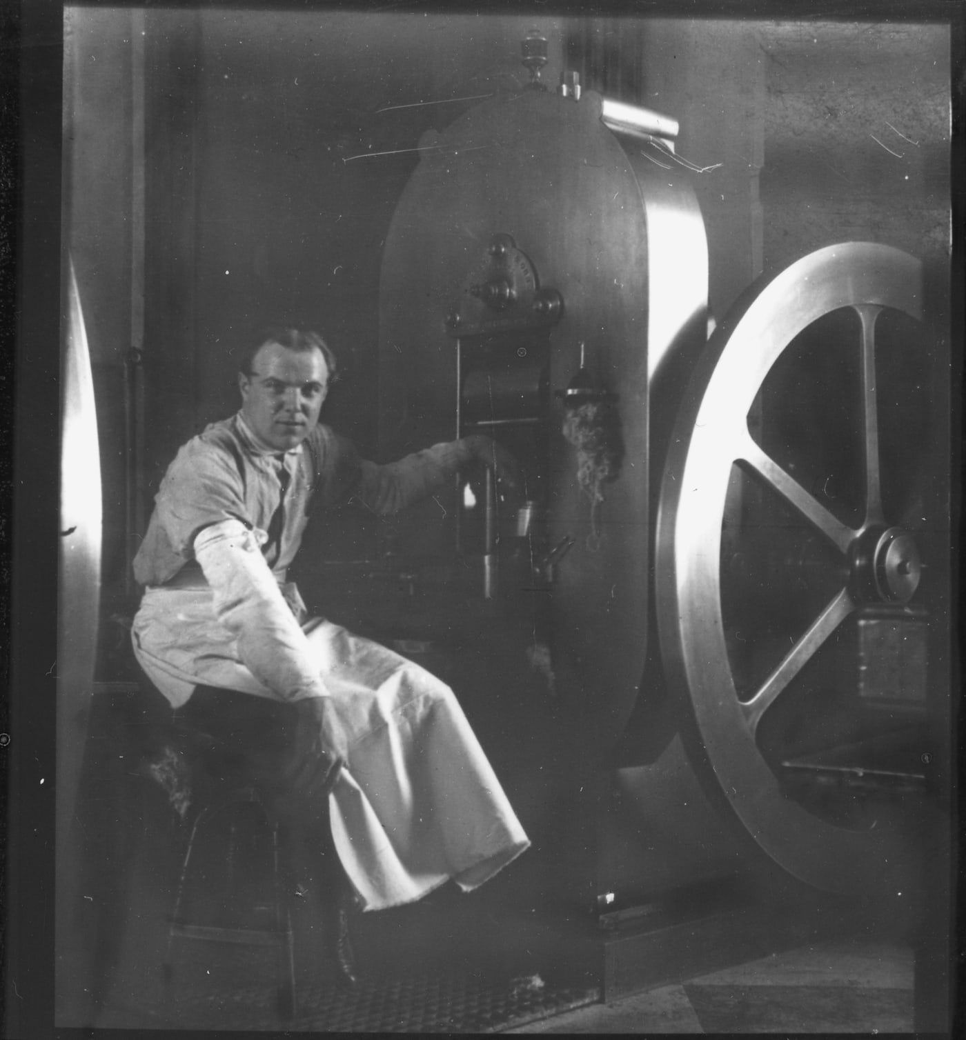 An operator sits beside a large mechanical coin press, surrounded by its metal frame, wheels and working parts.
