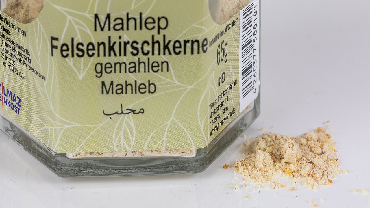 标有 Mahlep、装着磨碎樱桃仁的玻璃罐近景，旁边是一小堆浅色粉末。