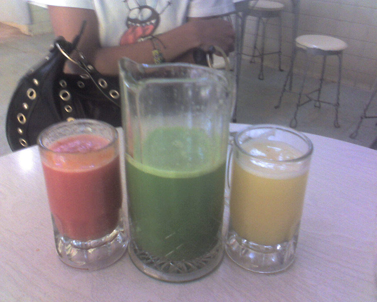 Three glasses of differently colored pulque arranged together on a table.