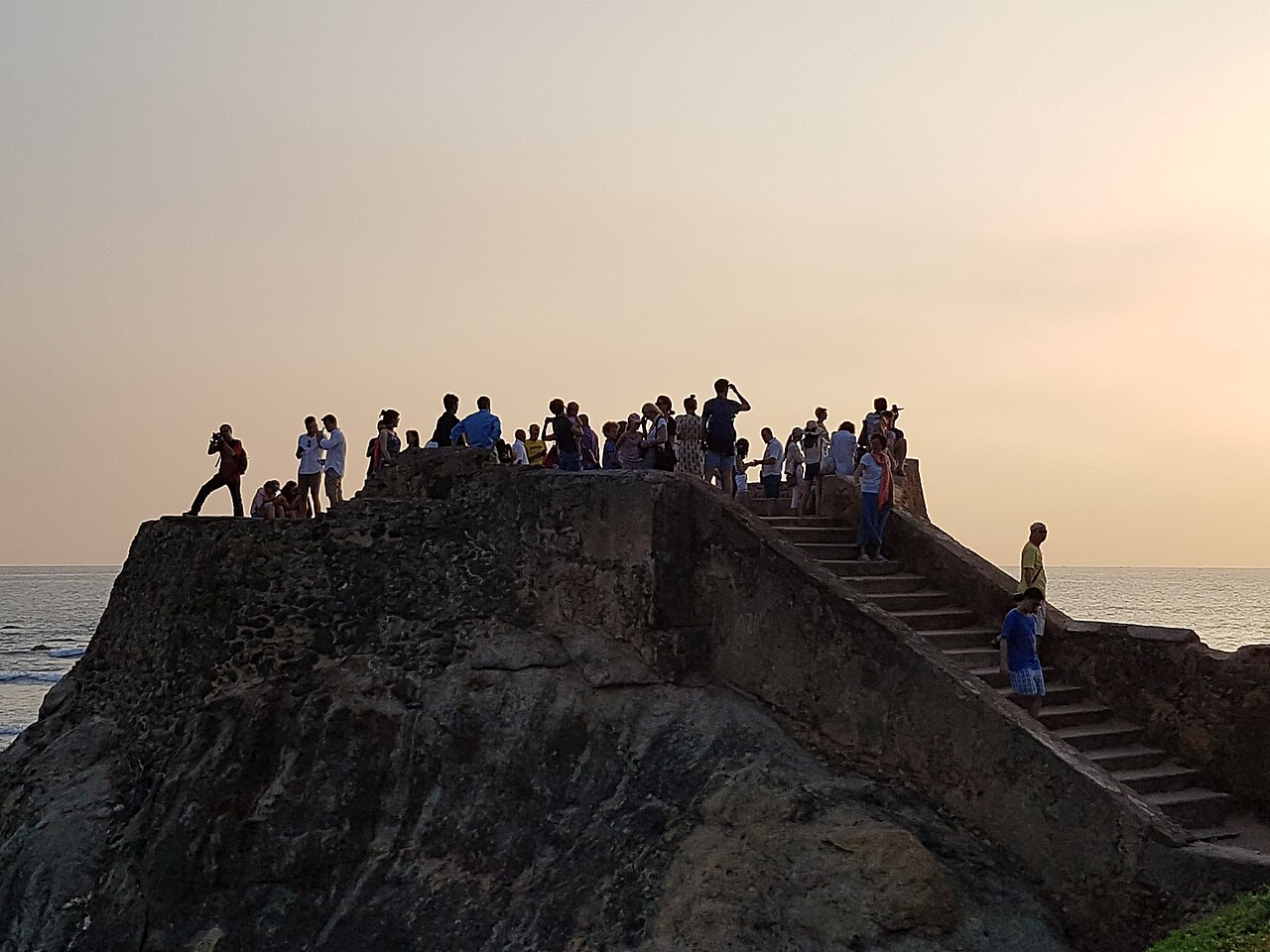 People gathered on the stone platform of Flag Rock Bastion above the sea at sunset in Galle.