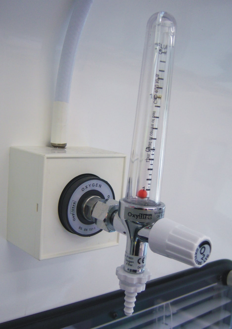A graduated oxygen flowmeter and white control knob connected to an oxygen outlet on an ambulance wall.