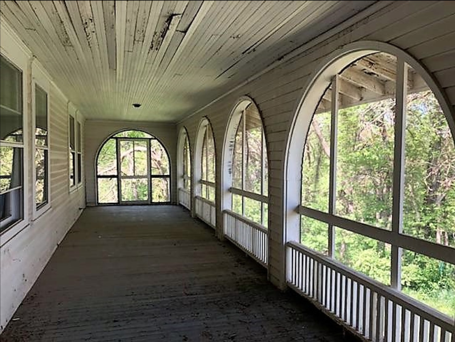 The long screened porch of the Picotte hospital, with repeated arched openings looking out toward trees.