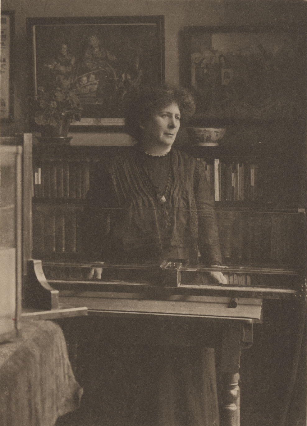Hertha Ayrton standing behind a glass ripple tank in a room lined with books and framed pictures.