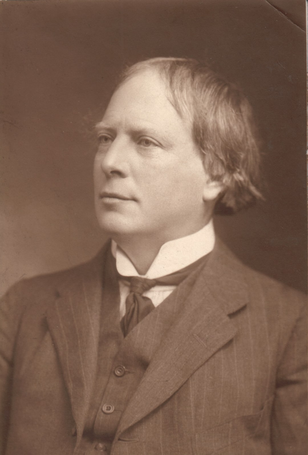 Sepia photographic portrait of Arthur Machen in a dark suit and high white collar, looking to the left.