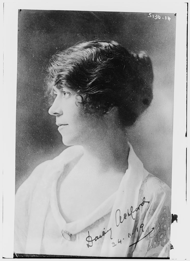 Archival portrait of the adult Daisy Ashford wearing a patterned dress, with her signature and a handwritten date across the lower part of the photograph.