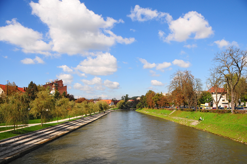 Long stone terraces and willow trees line the left side of the Ljubljanica at Trnovski pristan, opposite a grassy bank.