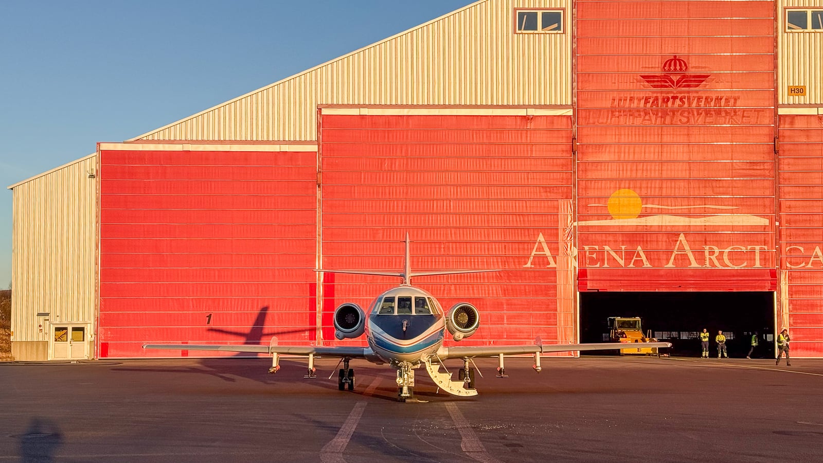 DLR's Falcon 20E research aircraft faces the camera outside the red doors of the Arena Arctica hangar, with instrument pods under its wings.