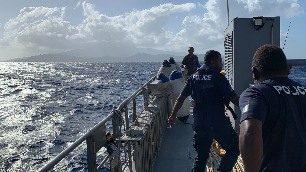 Police crew aboard RSIPV Gizo prepare a towline, with a mountainous island visible across the sea.