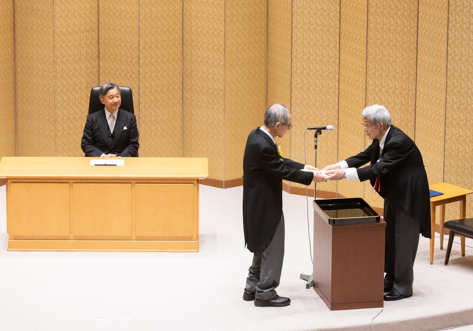 Kenso Soai receiving his Japan Academy Prize while the Emperor sits at a desk to the left, against a gold-patterned wall.