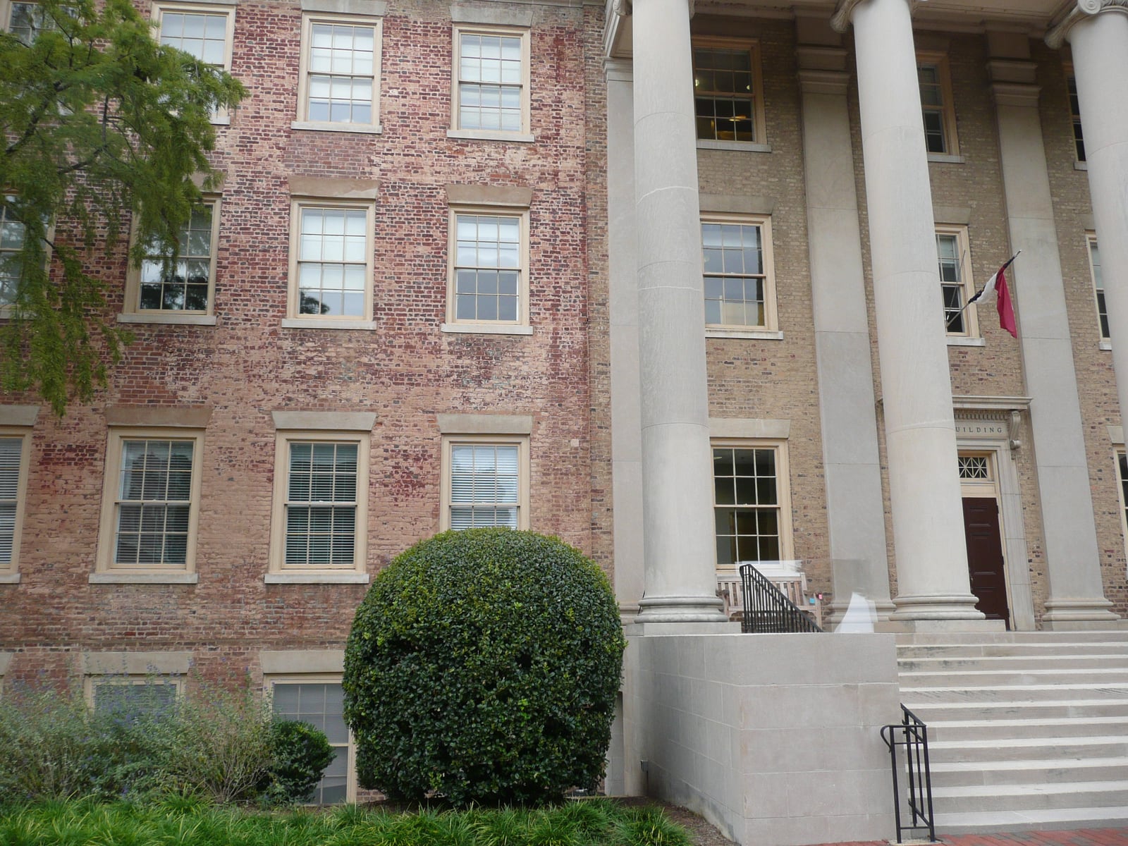 Weathered brickwork, repeated sash windows, and tall pale columns on South Building at UNC Chapel Hill, with steps and shrubs in the foreground.