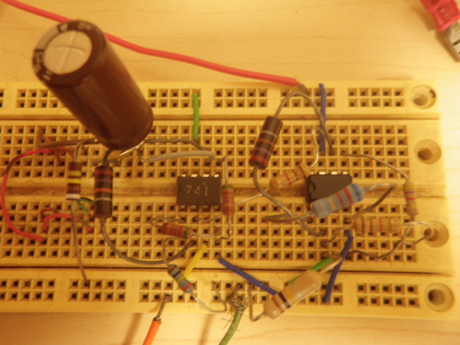 Two integrated circuits, resistors, colored jumper wires, and an electrolytic capacitor assembled on a white solderless breadboard.