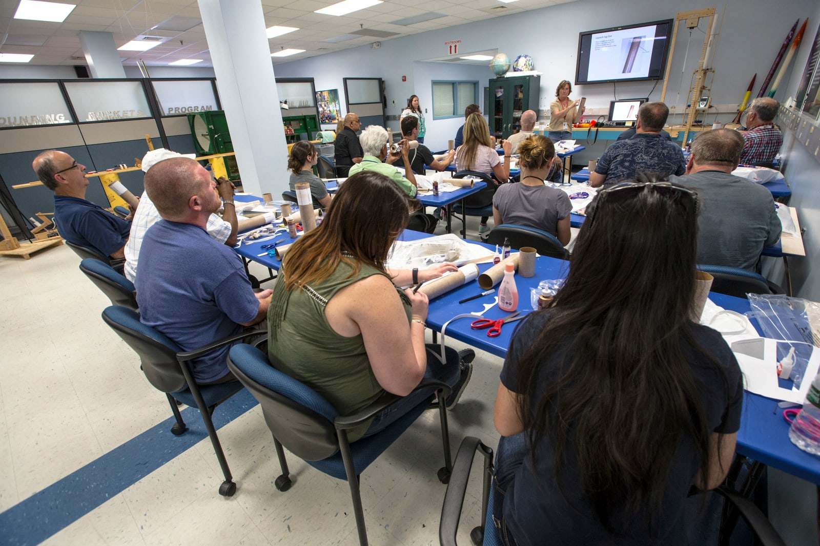 Teachers handle cardboard rocket parts at blue workshop tables during a demonstration at NASA Wallops.