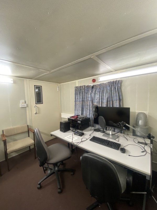 A microphone and circular pop filter extend over a desk with a monitor and keyboard inside Cambridge’s sound-treated phonetics recording booth.
