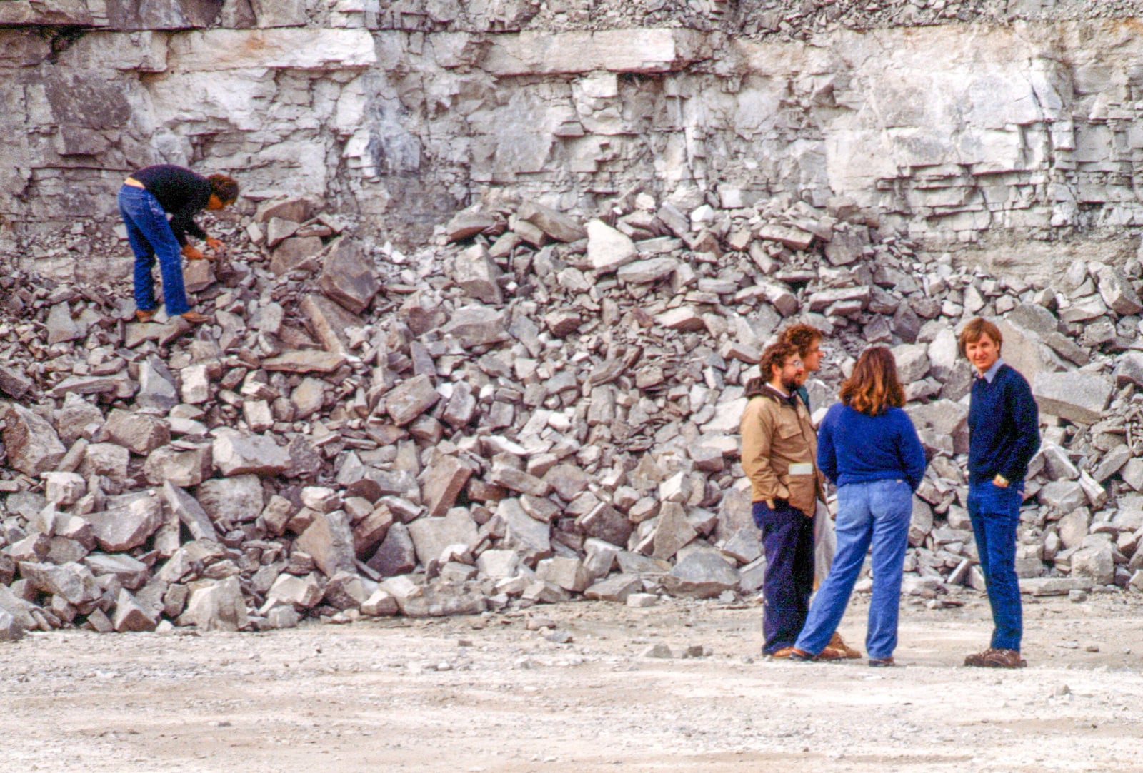Four members of a collecting team among pale, broken rock slabs beneath the layered wall of the Waukesha quarry.