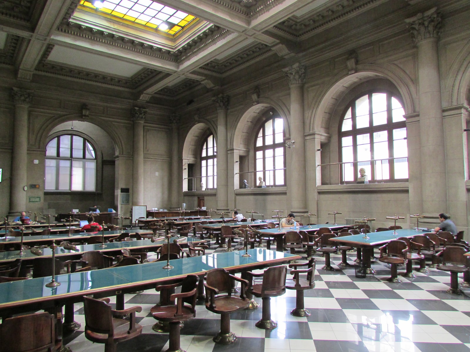 Green-topped reading tables, wooden chairs and arched windows under a stained-glass skylight in the Sala Gabriela Mistral, Santiago’s Biblioteca Nacional.