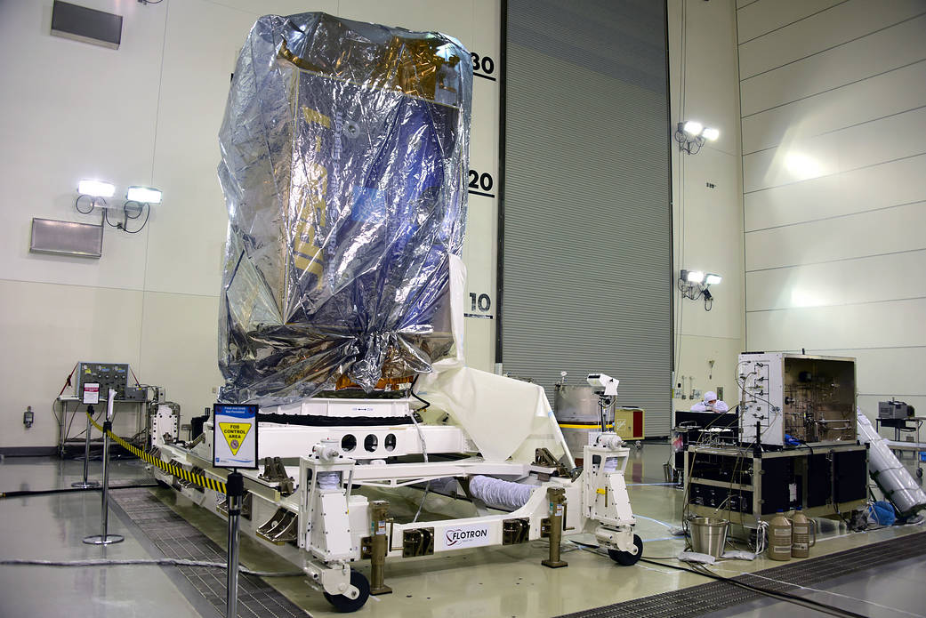 The silver-wrapped JPSS-1 spacecraft stands on wheeled support equipment inside a satellite processing facility.