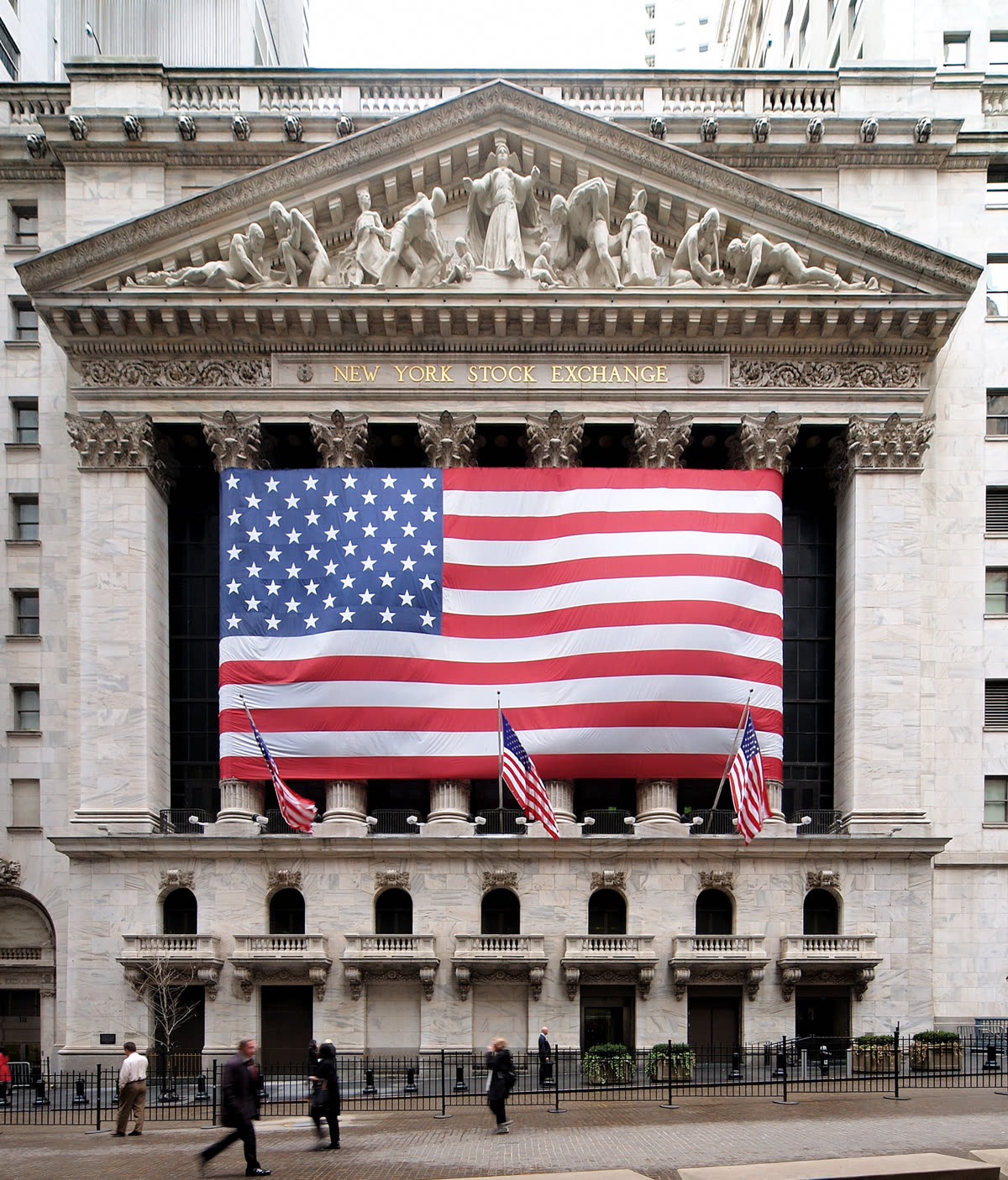 华尔街纽约证券交易所外立面，柱廊之间悬挂着一面大型美国国旗。