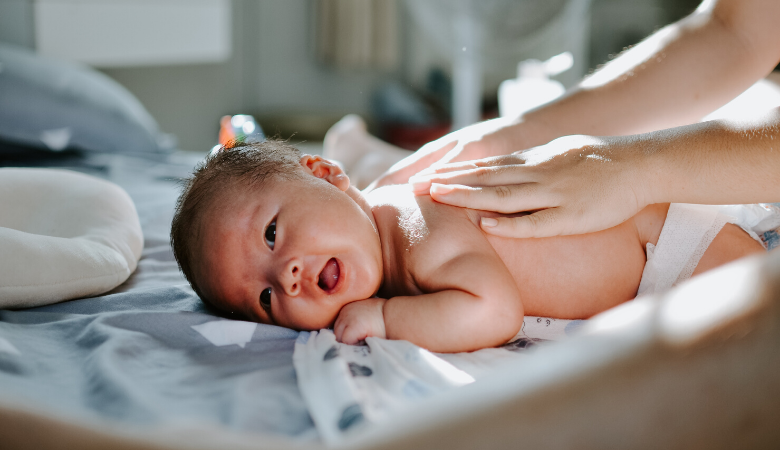 A caregiver rubs a baby's back as the baby lies on a bed.