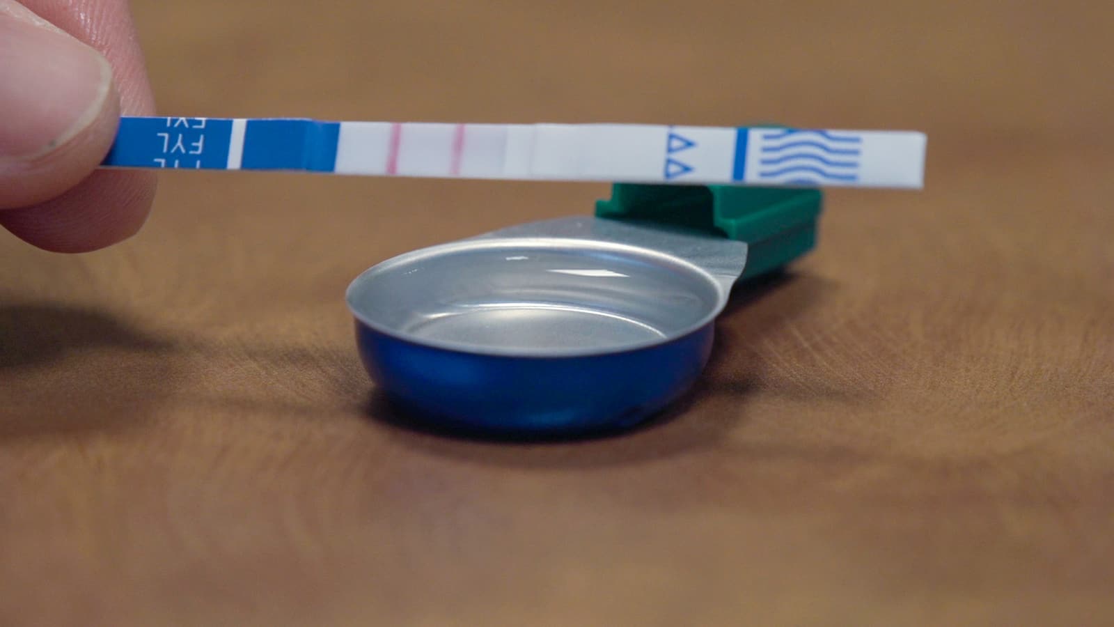 Close-up photograph of a fentanyl test strip held above a small metal cup.