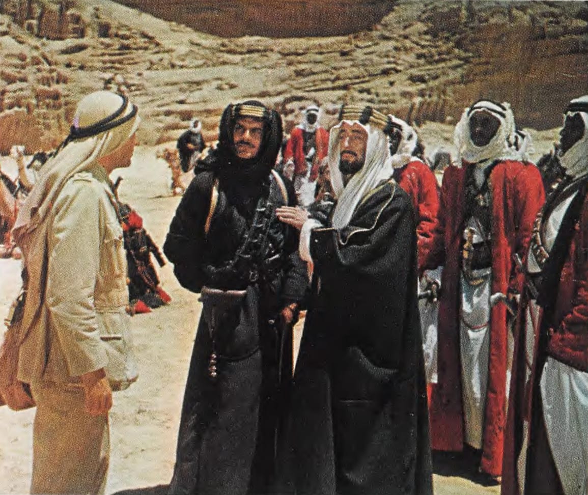 Archival film-publicity still from Lawrence of Arabia showing Alec Guinness and Omar Sharif in costume against a desert setting.
